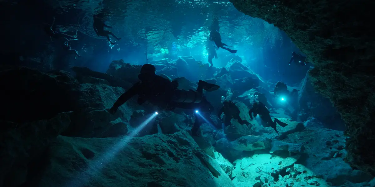 Group of certified divers exploring the Chikin Ha cenote cavern with dive lights