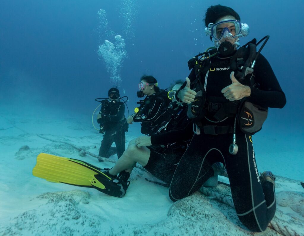 Group of scuba divers kneeling on sandy bottom waiting for bull sharks in Playa del Carmen