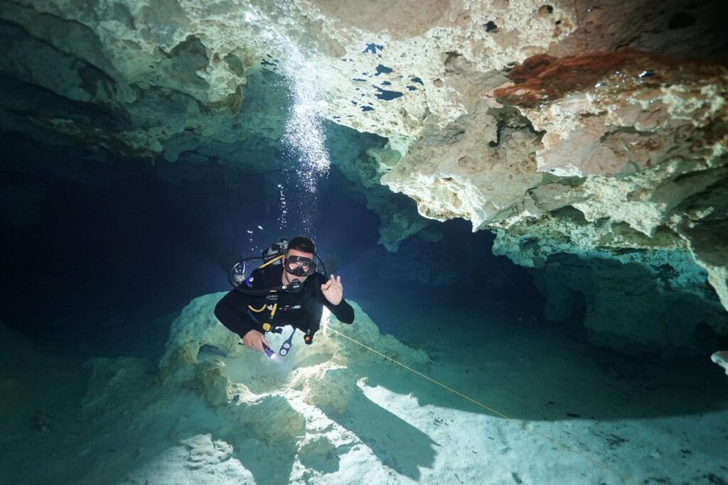Buzo suspendido en la caverna iluminada de Dos Ojos con burbujas subiendo hacia el techo