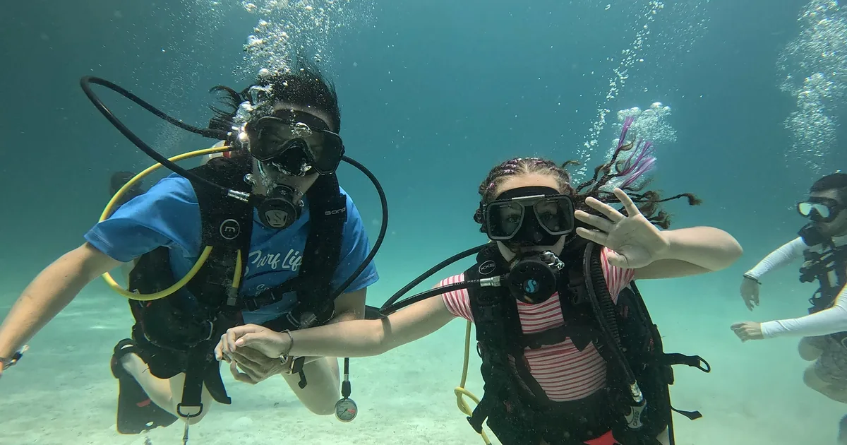 Participante saludando bajo el agua junto a su acompañante en su primer buceo en Playa del Carmen