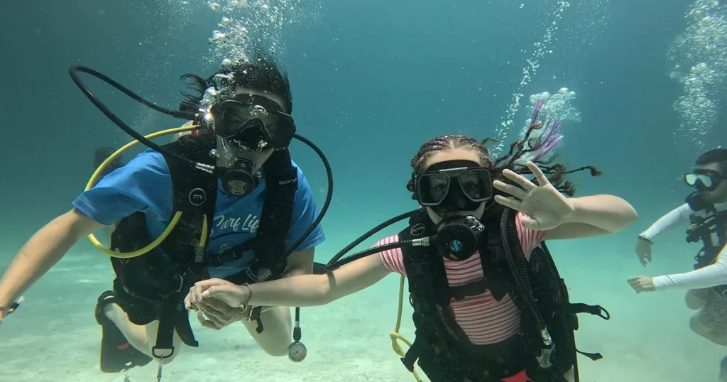 First-time diver waving underwater next to a dive companion in Playa del Carmen